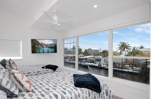 A bedroom with a large window overlooking a marina, a ceiling fan, and a bed with patterned bedding.