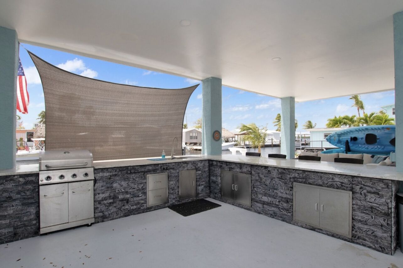 An outdoor kitchen with a gas stove, cabinets, and a large shade cloth.
