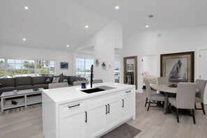 Une cuisine moderne avec des meubles blancs, un îlot central doté d’un évier et un coin repas avec une table ronde et des chaises.