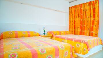 A room with two beds, each with a floral bedspread, a nightstand, and a window with orange curtains.