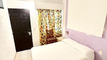 Una habitación con cama, ventilador de techo, puerta y cortina estampada con motivos florales.