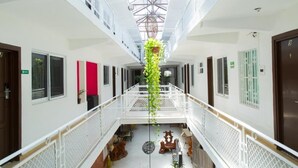 Un couloir d’hôtel avec un atrium central, des murs blancs et une plante suspendue.
