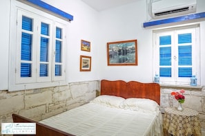 Una camera da letto con una testiera in legno, un letto con lenzuola bianche, due quadri appesi alla parete e una finestra con persiane blu.