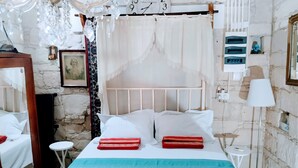 A bed with white linens and red and blue pillows, a small bedside table, a lamp, and a wall clock.
