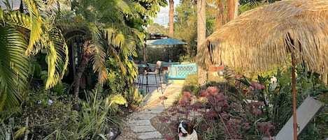 Un jardín tropical con sillones de descanso, una sombrilla de paja y un sendero de piedra.