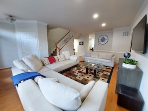 Ein modernes Wohnzimmer mit einem großen Ecksofa, einem Couchtisch und einer Treppe, die zu einer oberen Etage führt.