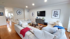 A modern living room with a sofa, a coffee table, and a TV. There is a dining area in the background. - Stunning 2400 Sqft. 4 BR, 3.5 BT in the most convenient location to Quantico (Stafford)