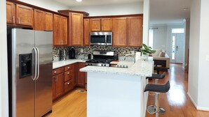 A modern kitchen with wooden cabinets, stainless steel appliances, and a central island with bar stools. - Stunning 2400 Sqft. 4 BR, 3.5 BT in the most convenient location to Quantico (Stafford)