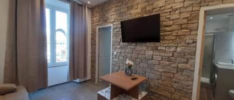 Una sala de estar moderna con una pared de piedra, un televisor de pantalla plana montado sobre una mesa de centro de madera, y un ventanal corredizo que da a un balcón.