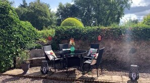 An outdoor patio with a round table and four chairs, surrounded by greenery and a stone wall. - New - Luxury Spacious Apartment in Beautiful Grounds (Oswestry, Shropshire)