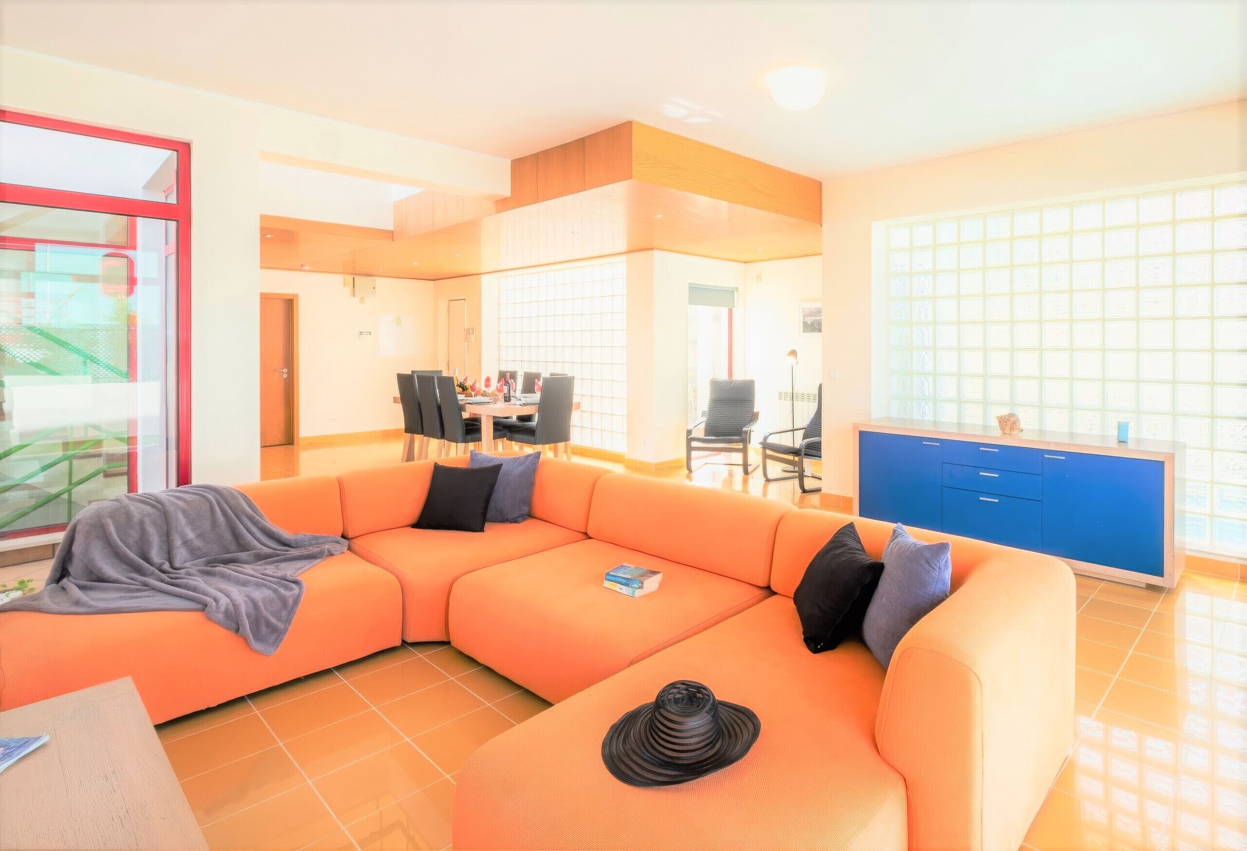 A modern living room with a sectional sofa, a dining area, and a kitchen with blue cabinets.