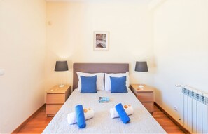 A hotel room with a bed, two bedside tables, a nightstand, a framed picture on the wall, and a radiator. - Villa with heatable pool & BBQ in Albufeira Marina (Albufeira)