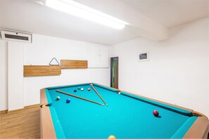 A pool table with balls and cues, a wooden bench, a white wall with a framed picture, and a door. - Villa with heatable pool & BBQ in Albufeira Marina (Albufeira)
