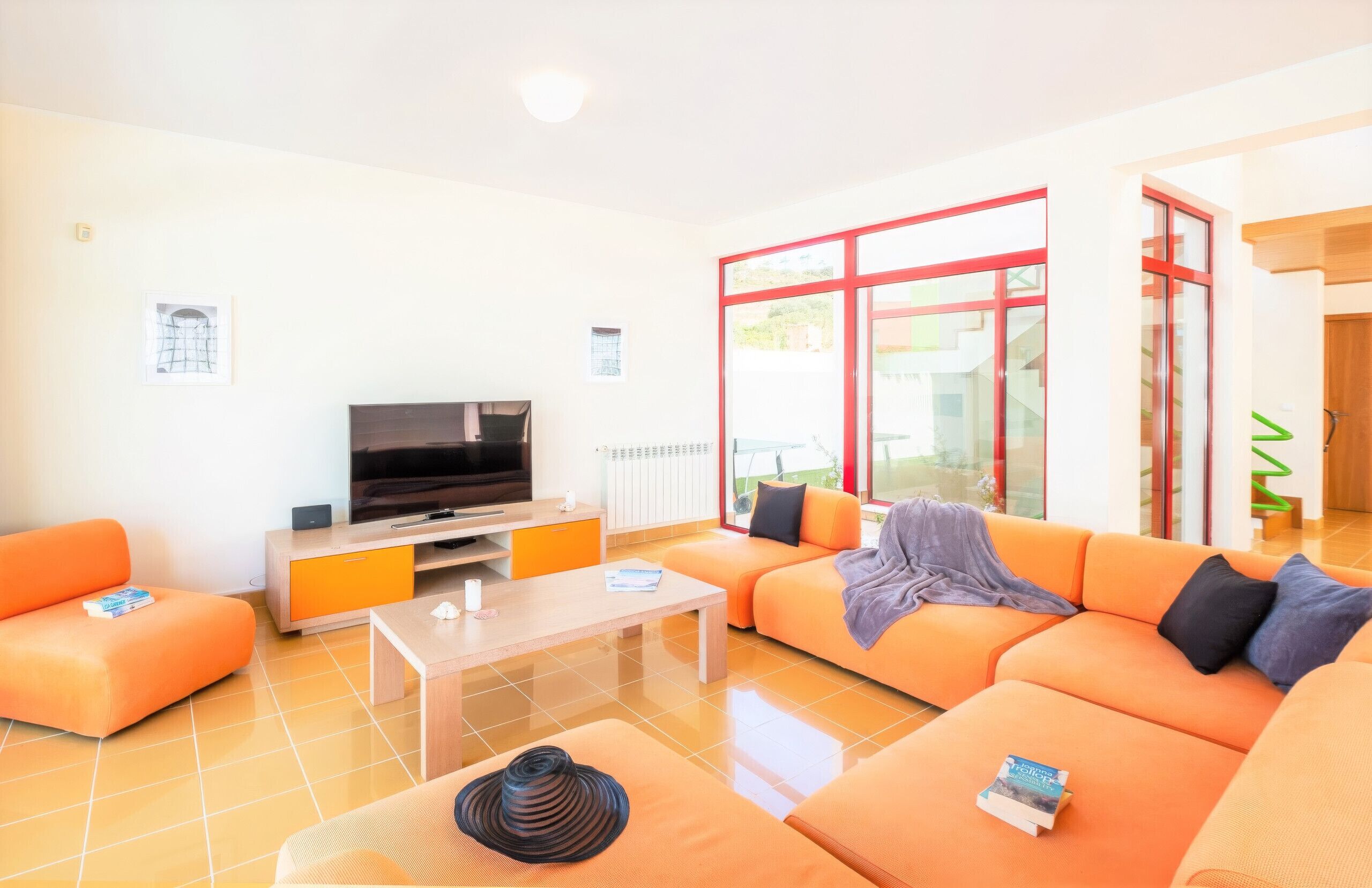 A modern living room with orange sofas, a flat-screen TV, and a coffee table.