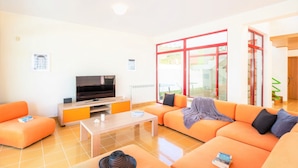 Ein modernes Wohnzimmer mit Flachbildfernseher, orangefarbenen Sofas, einem Couchtisch und einem großen Fenster mit roten Rahmentüren.