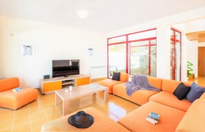 A modern living room with orange sofas, a flat-screen TV, and a coffee table. - Villa with heatable pool & BBQ in Albufeira Marina (Albufeira)