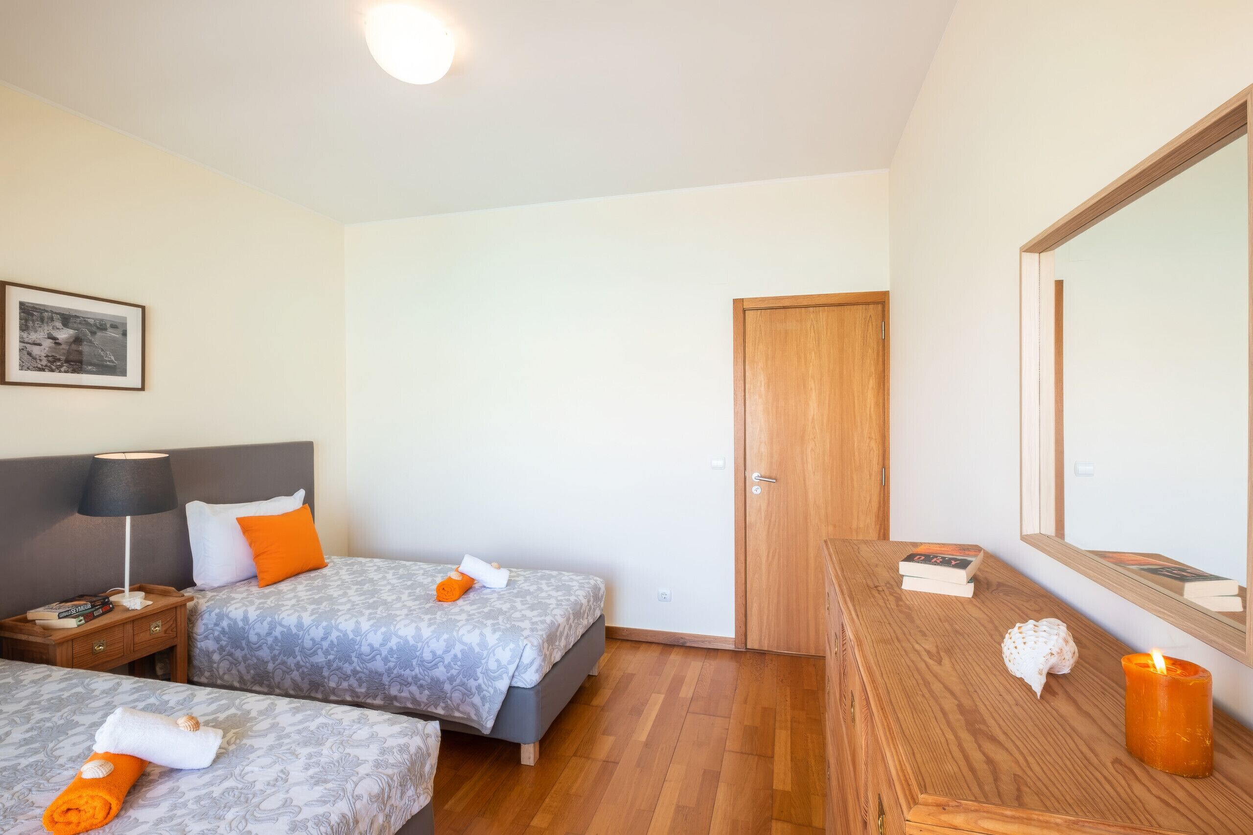 A hotel room with two beds, a wooden dresser, a nightstand, a framed picture on the wall, and a mirror.