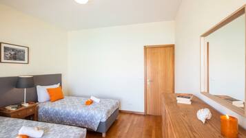 A hotel room with two beds, a wooden dresser, a nightstand, a framed picture on the wall, and a mirror.