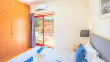 A hotel room with a bed, a nightstand, a lamp, a wardrobe, and a sliding glass door leading to an outdoor area.