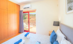 A hotel room with a bed, a nightstand, a lamp, a wardrobe, and a sliding glass door leading to an outdoor area.