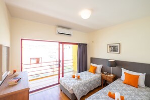 A hotel room with two beds, a desk, a chair, a window with a view, and an air conditioning unit.