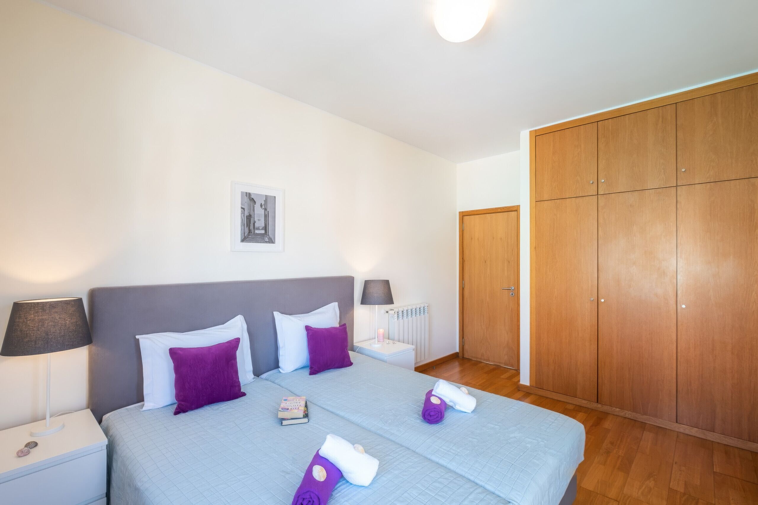 A bedroom with a bed, bedside lamps, a radiator, and a wardrobe.