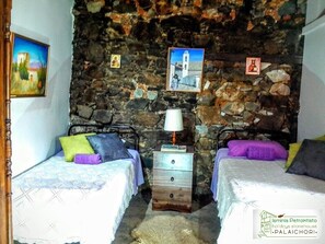 Una habitación con dos camas, una pared de piedra y una mesita con una lámpara.