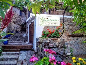 Una escalera de piedra lleva a una puerta con un cartel que indica Ismimis Petrokristo, alojamiento vacacional en Palaichori.