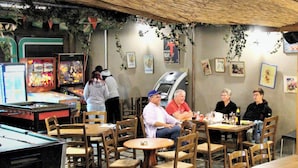 Ein gemütlicher Innenbereich mit Essbereich, Holztischen und -stühlen, einer Billardkugel und Spielautomaten.