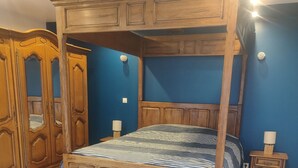 A four-poster bed with a patterned bedspread, wooden wardrobe, and bedside lamps in a room with blue walls and wooden flooring. - Gîte la bocagere  (Autreppes)