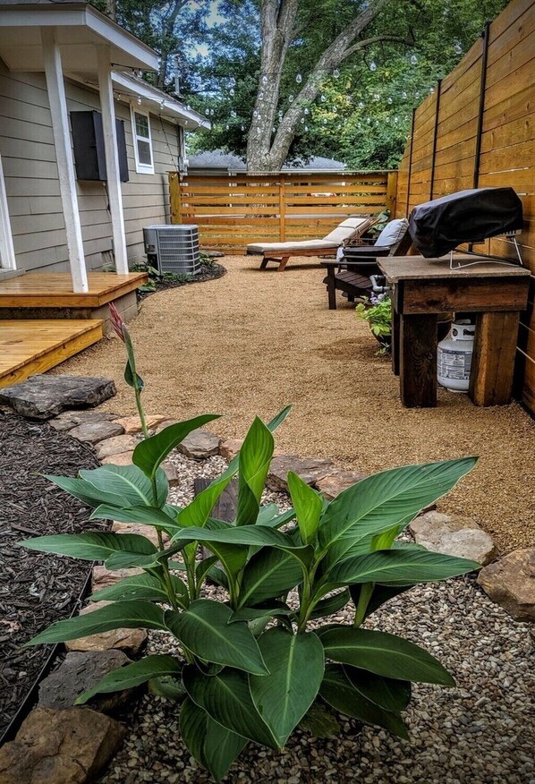 Een achtertuin met een houten terras, een barbecue en een zithoek met een tafel en stoelen.