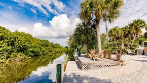 A wooden dock extending into a calm river, surrounded by lush greenery and palm trees. - Designer Home on a Canal (Siesta Key)