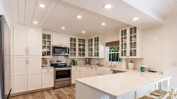 A modern kitchen with white cabinetry, a central island, and built-in appliances. - Designer Home on a Canal (Siesta Key)