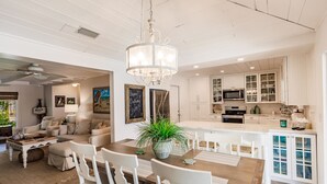 A spacious living room with a wooden dining table, white chairs, and a chandelier. - Designer Home on a Canal (Siesta Key)