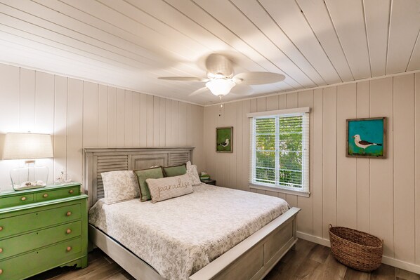A bedroom with a bed, a nightstand, a dresser, a ceiling fan, a window, and a wall-mounted picture. - Designer Home on a Canal (Siesta Key)