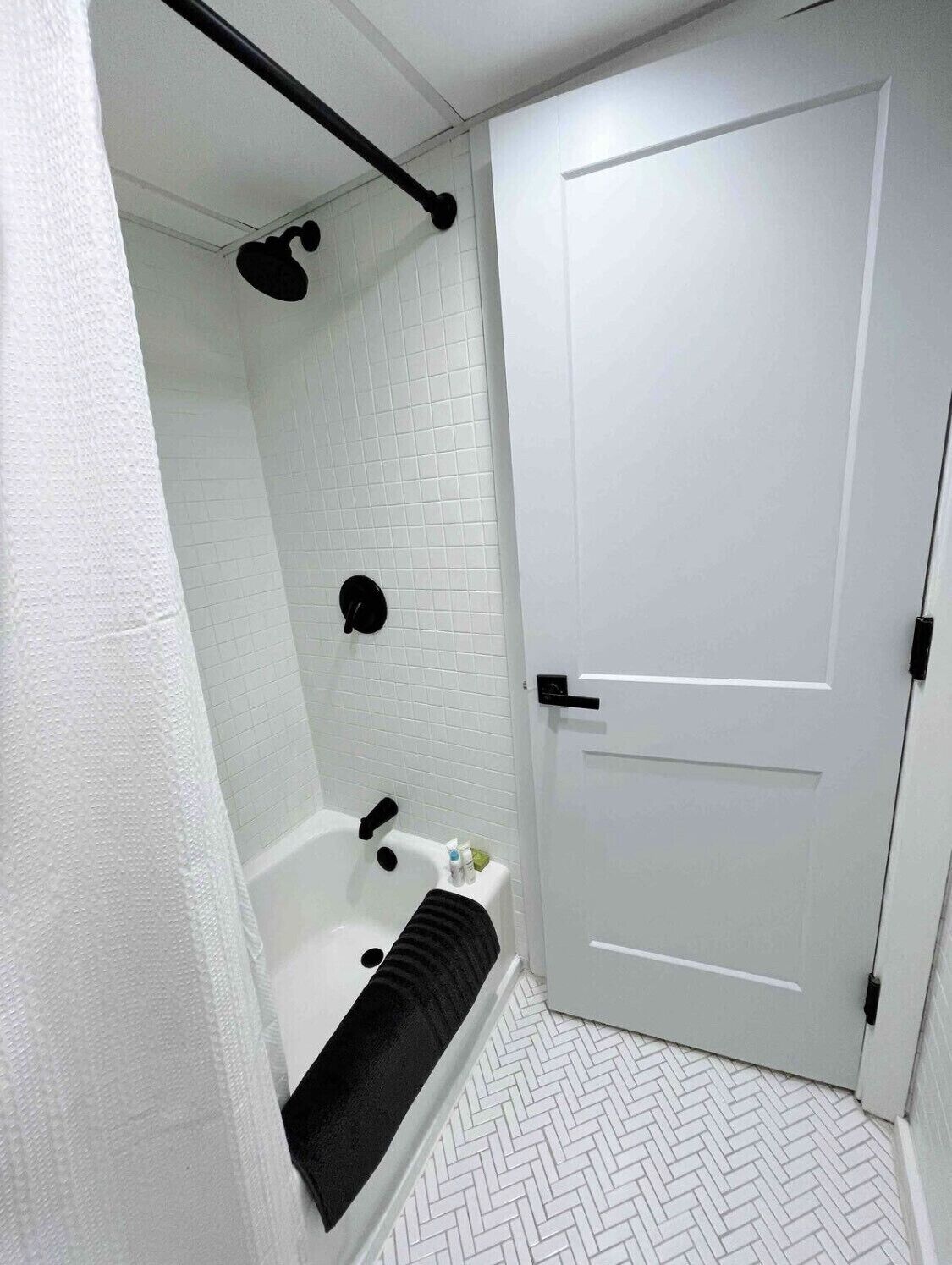 A bathroom with a white tiled shower, a black towel, and a white door.
