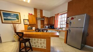 A kitchen with a central island, wooden cabinets, a refrigerator, and a painting on the wall. - Private Guest Villa - Two Bedroom - Full Kitchen - Ocean Front Villa Cozumel (San Miguel de Cozumel)