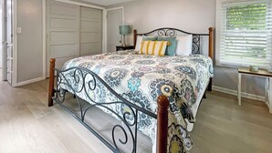 A bedroom with a bed, a nightstand, a lamp, a window with blinds, and a door. - Pet Friendly Home by Lake Shawnee! (Topeka)