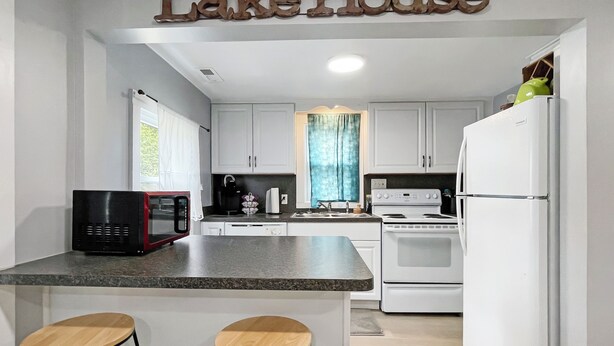 A kitchen with white cabinets, a stove, a microwave, and two wooden stools. - Pet Friendly Home by Lake Shawnee! (Topeka)