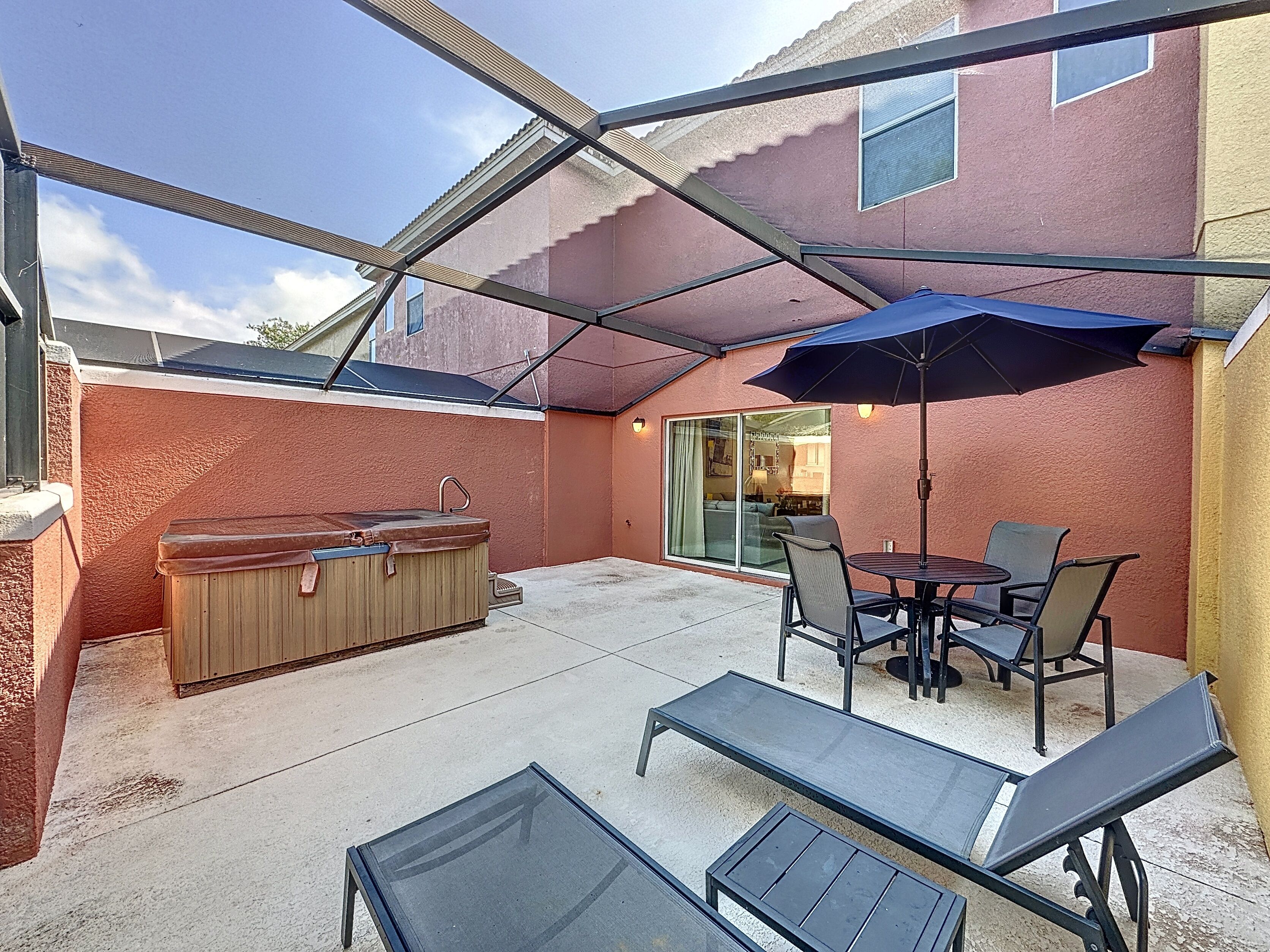 A covered patio area with a hot tub, outdoor seating, and a glass door leading to an interior space.
