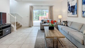 Una sala de estar moderna con una televisión de pantalla plana, un sofá, una mesa de centro con flores y una escalera que lleva a un área exterior.