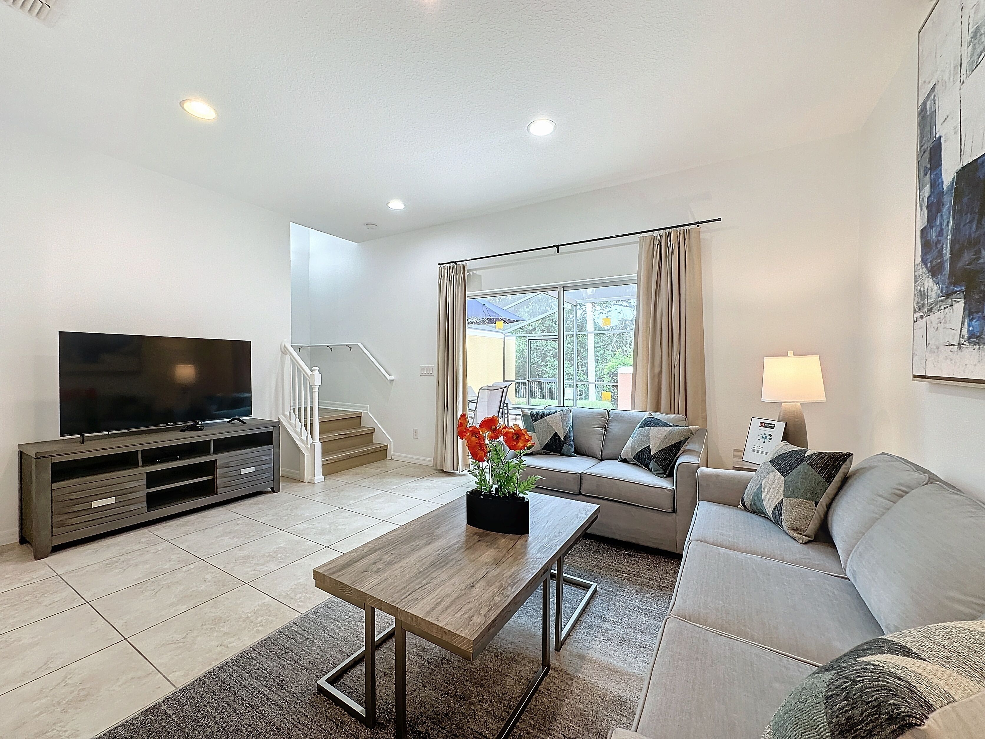 A modern living room with a flat-screen TV, a wooden coffee table, a sofa, and a staircase leading to an outdoor area.