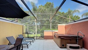 Un espacio exterior techado con jacuzzi, asientos y cerramiento de vidrio.