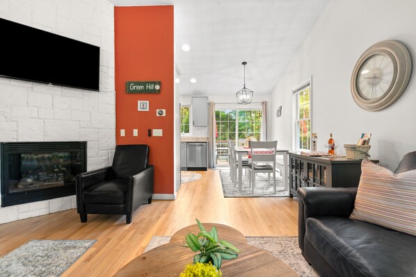 Un salon moderne avec une cheminée, un canapé en cuir noir et un coin repas comprenant une table et des chaises.