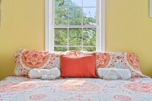 Un lit avec une literie à motifs floraux, une fenêtre donnant sur des arbres et un mur jaune.