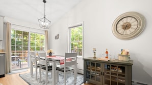 Un comedor con una mesa dispuesta para cuatro, un armario gris con puertas de cristal y un reloj de pared grande.