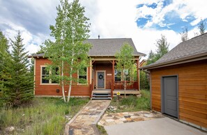 A wooden house with a front porch, stone pathway, and a small garden.