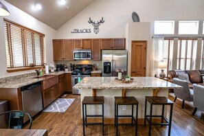 A modern kitchen with wooden cabinets, stainless steel appliances, and a granite island with bar stools.