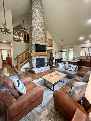 A spacious living room with a stone fireplace, leather sofas, and a wooden staircase.