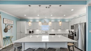 Una cocina moderna con una isla grande, armarios blancos, electrodomésticos de acero inoxidable e iluminación colgante.